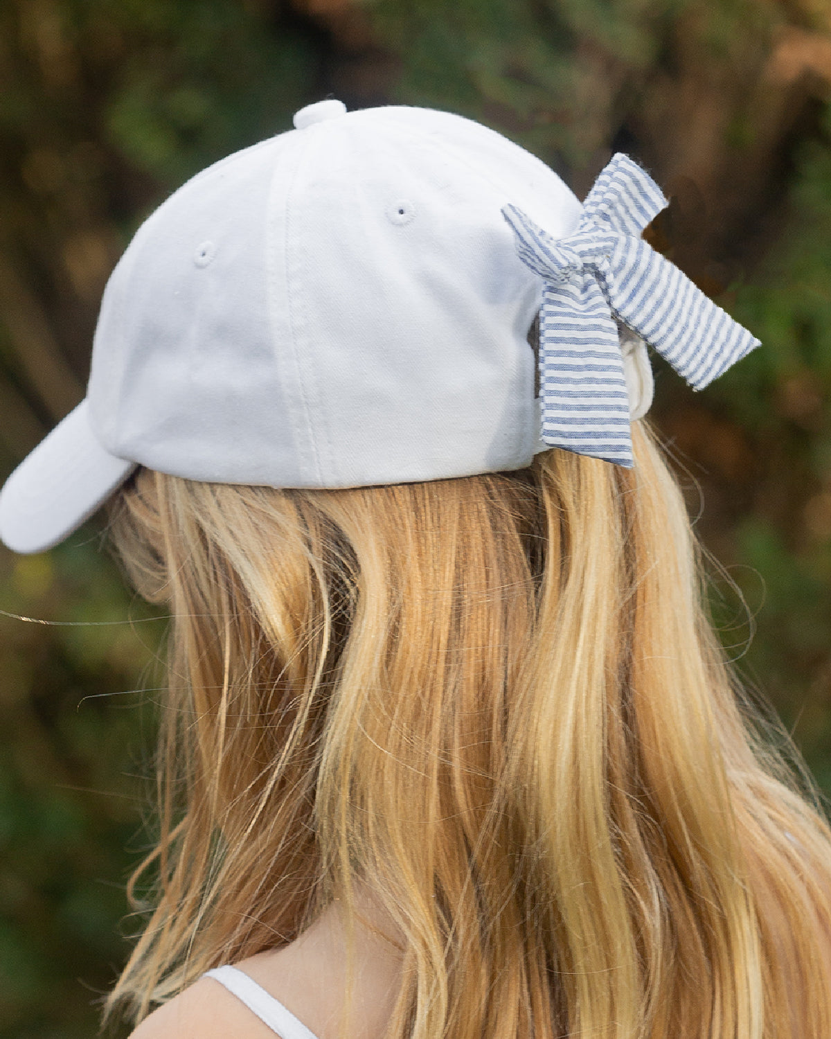 Teen girl wearing white baseball hat with blue and white bow on the back