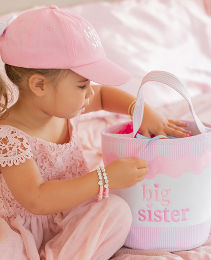 Girl wearing pink big sister hat, big sister bracelet and next to a big sister tote bag