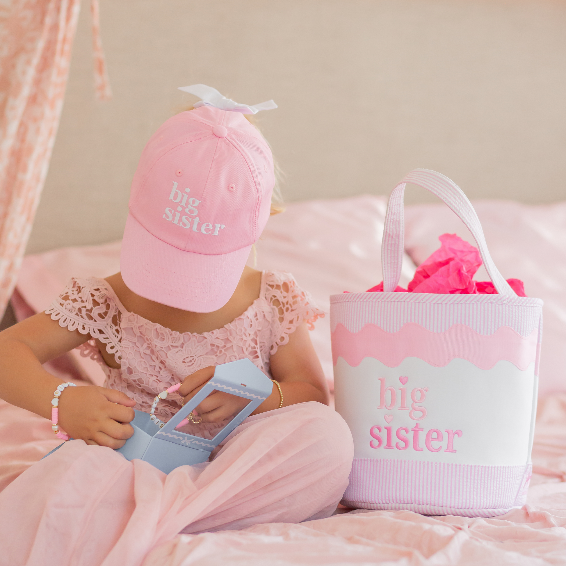 Girl wearing pink big sister hat, big sister bracelet and next to a big sister tote bag