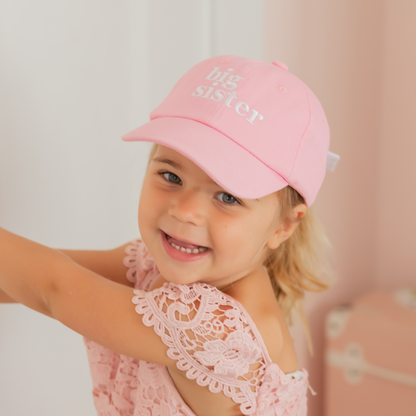 Girl wearing a pink baseball hat with Big Sister embroidery and bow on the back