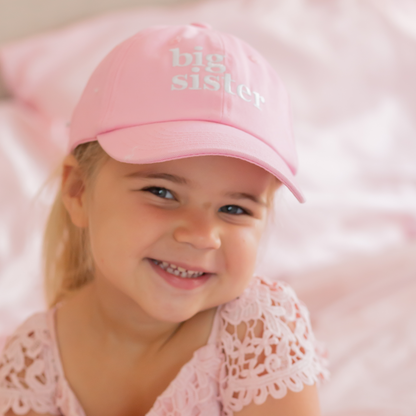 Girl wearing a pink baseball hat with Big Sister embroidery and bow on the back