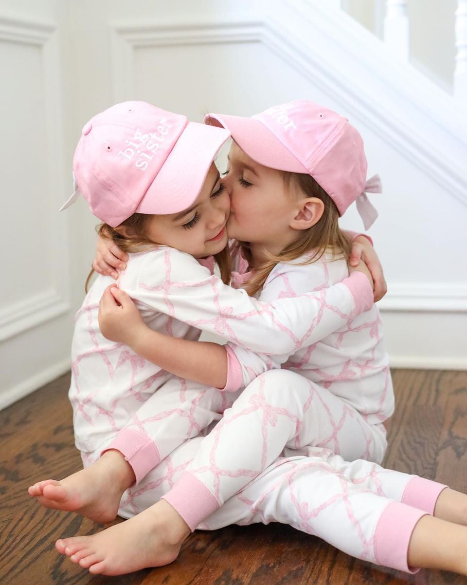 Sisters wearing matching pink baseball hats with bows on the back