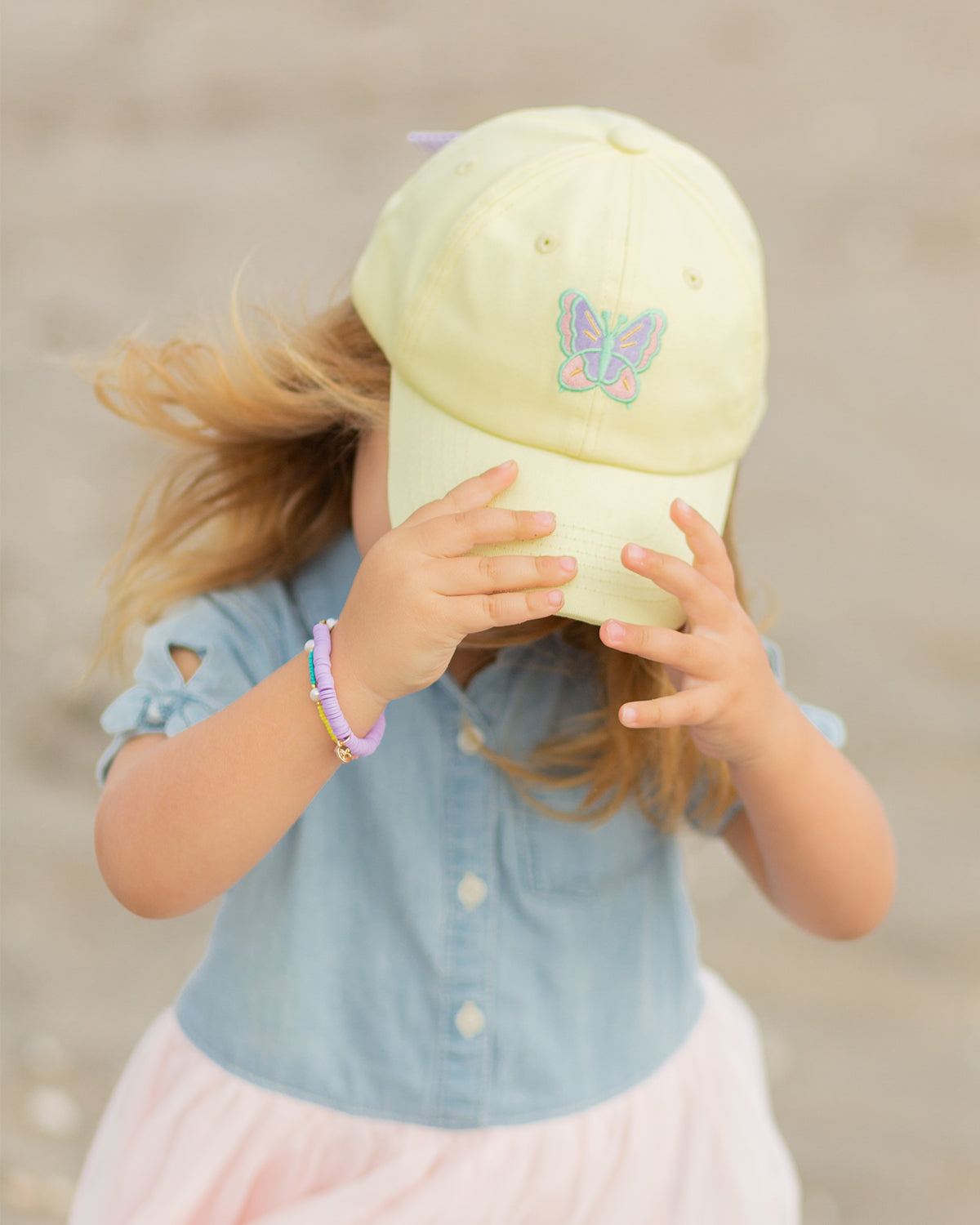 Girl wearing a yellow baseball hat with butterfly embroidery and bow on the back