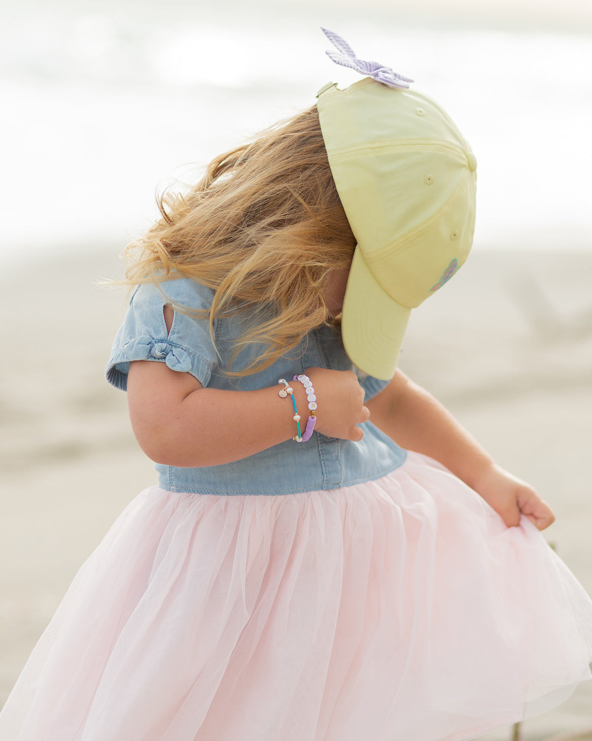 Girl wearing a yellow baseball hat with butterfly embroidery and bow on the back