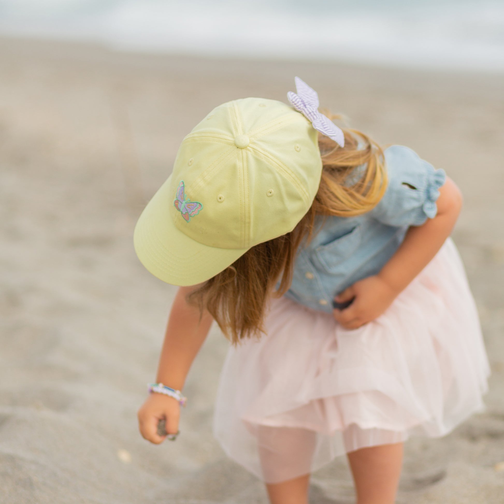 Girl wearing a yellow baseball hat with butterfly embroidery and bow on the back