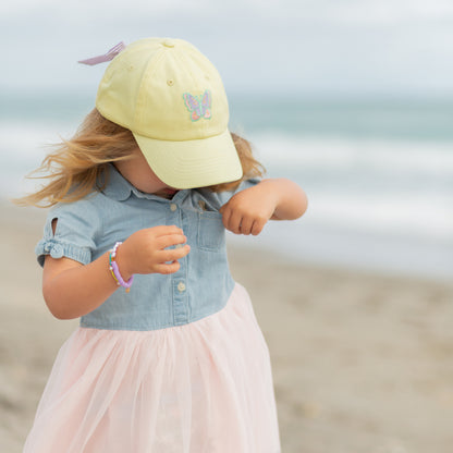 Girl wearing a yellow baseball hat with butterfly embroidery and bow on the back