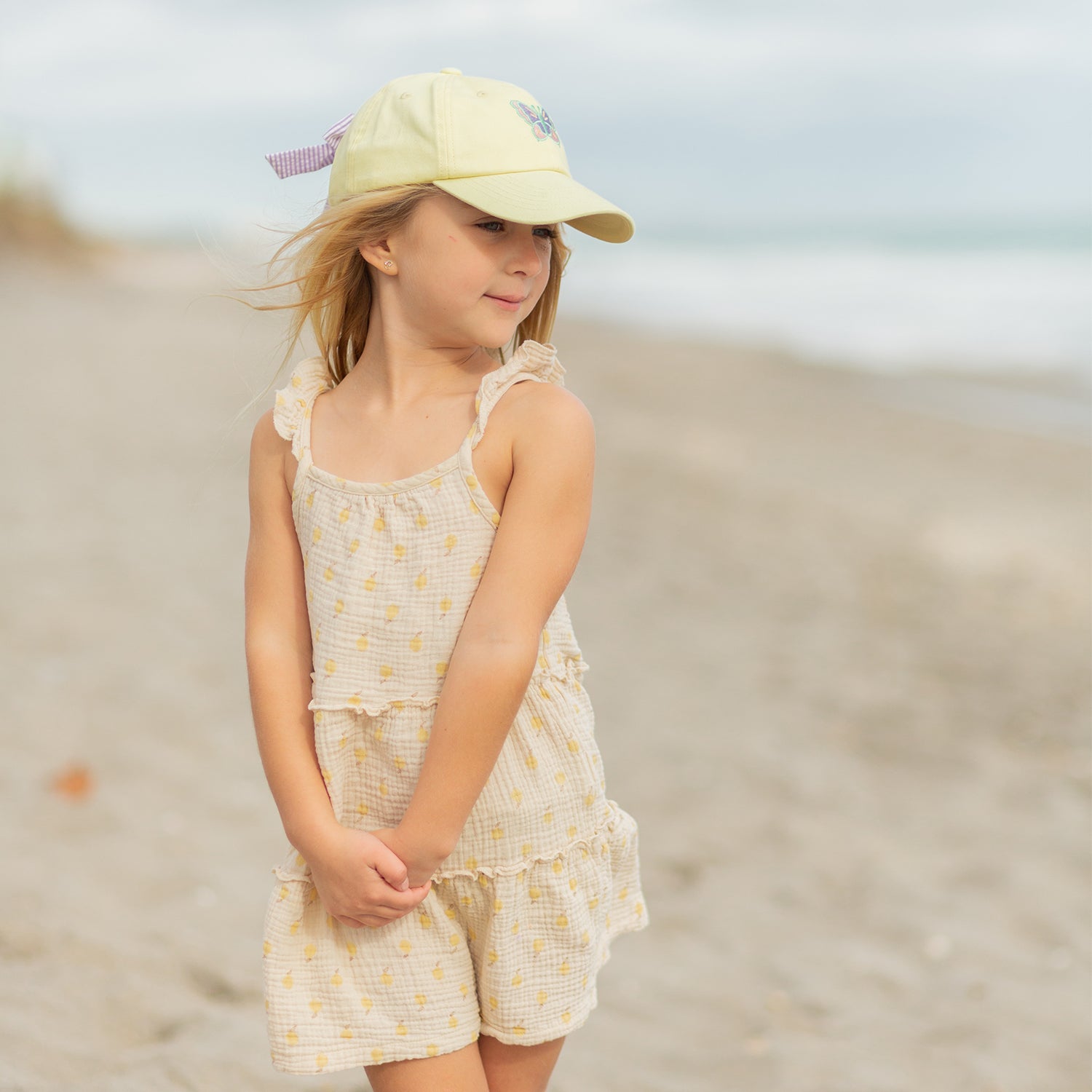 Girl wearing a yellow baseball hat with butterfly embroidery and bow on the back