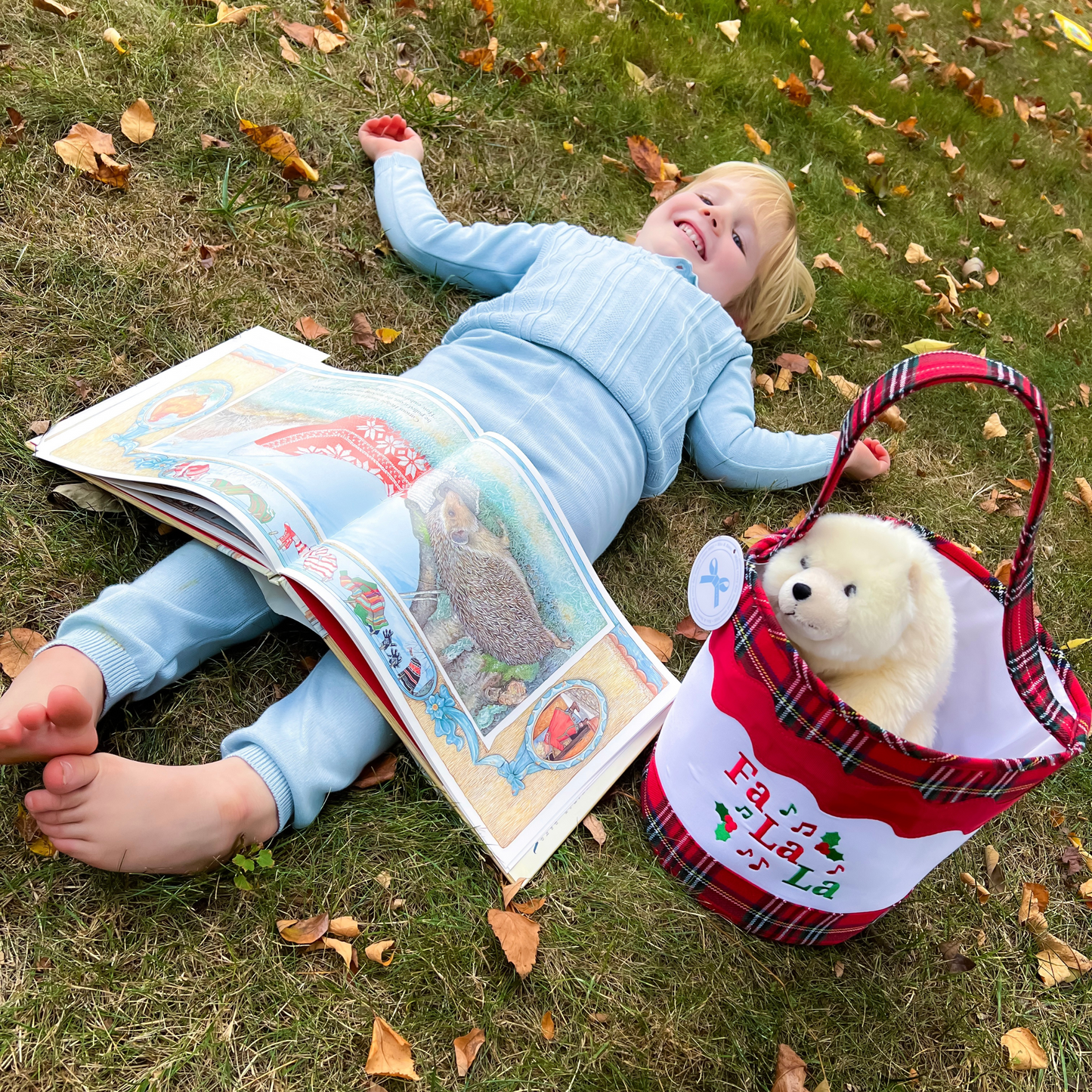 Boy laying next to a red plaid Christmas tote bag with Fa la la embroidery on it