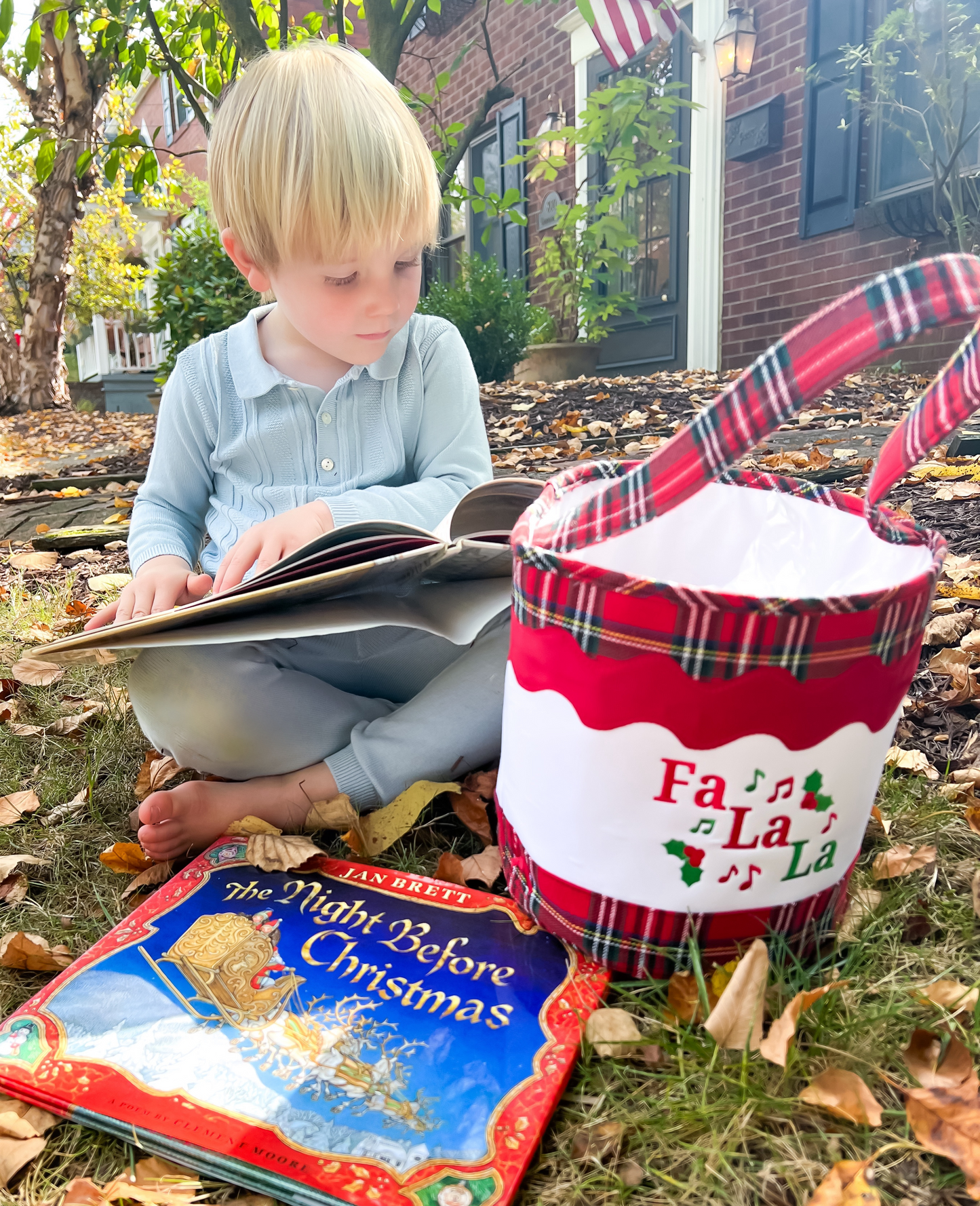 Boy reading books next to a red plaid Christmas tote bag with Fa la la embroidery on it