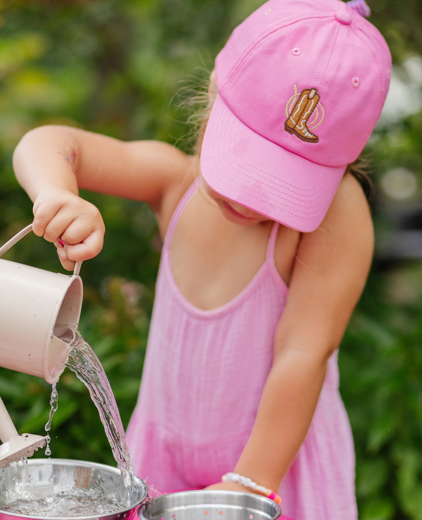 Girl wearing magenta baseball hat with cowboy boot embroidery and a bow on the back