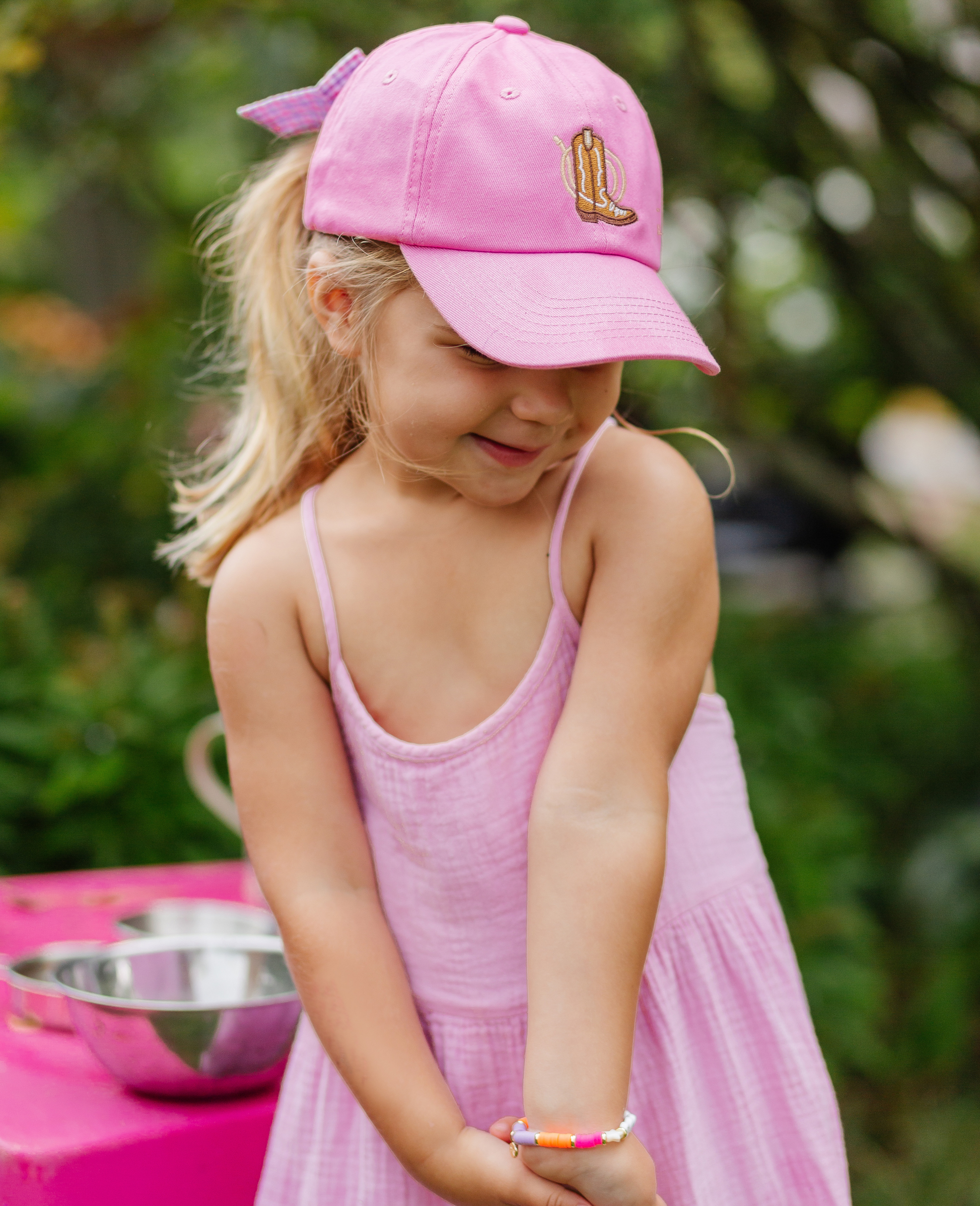 Girl wearing magenta baseball hat with cowboy boot embroidery and bow on the back