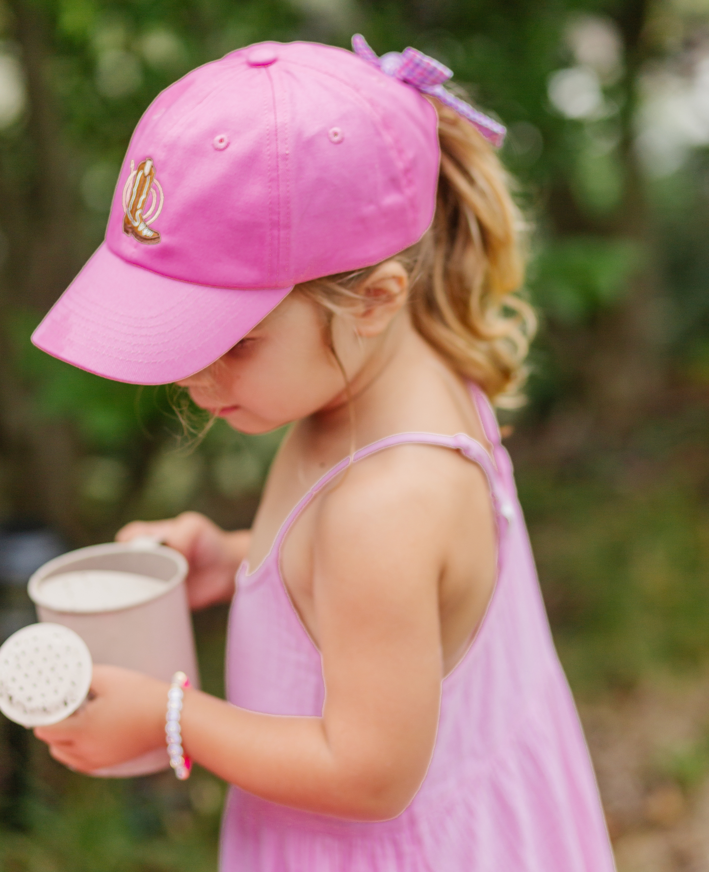 Girl wearing magenta baseball hat with cowboy boot embroidery and bow on the back