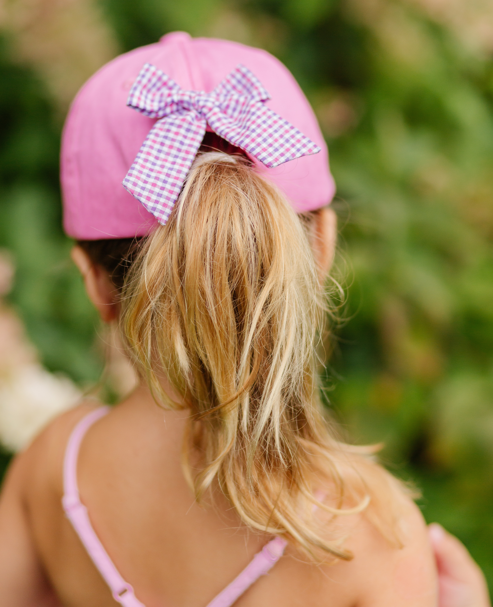 Girl wearing magenta baseball hat with bow on the back