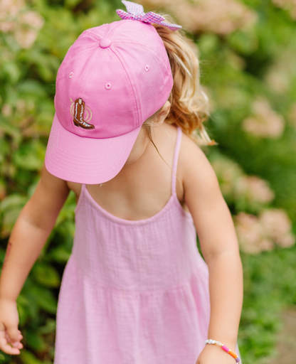 Girl wearing magenta baseball hat with cowboy boot embroidery and bow on the back