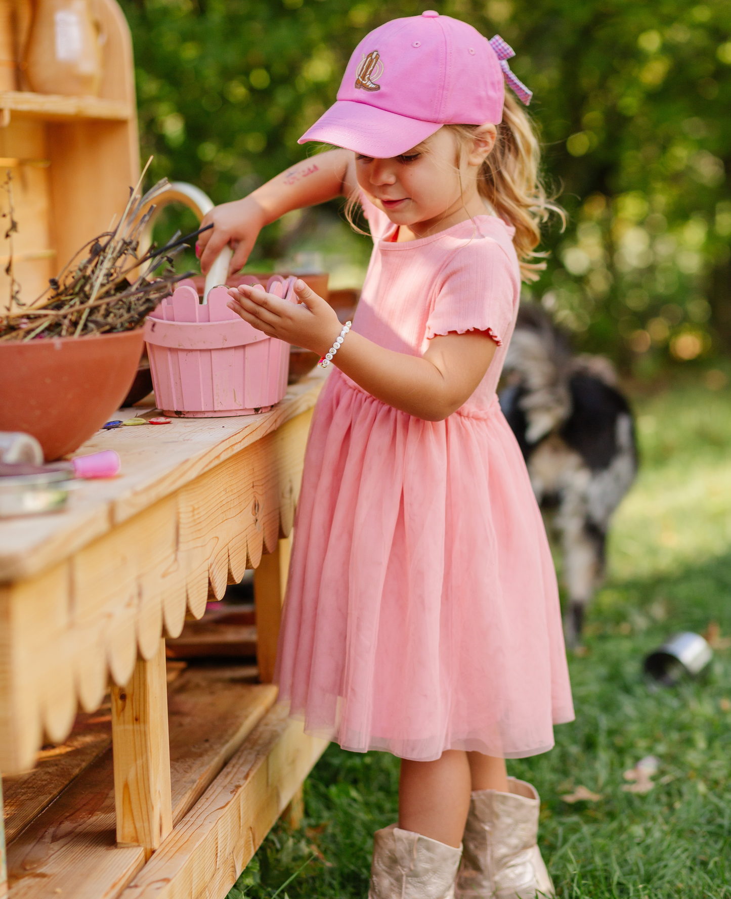 Girl wearing magenta baseball hat with cowboy boot embroidery and bow on the back