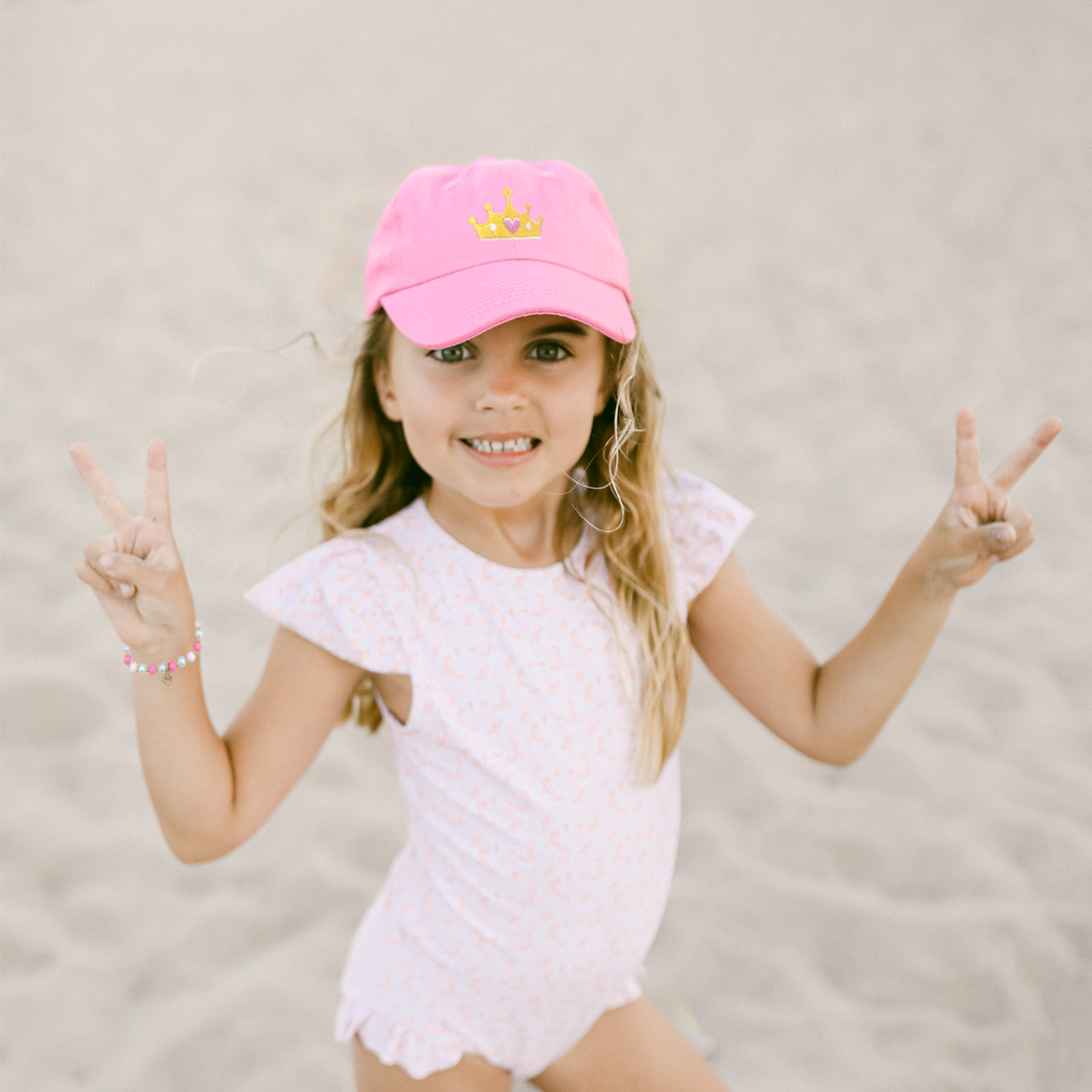 Girl wearing a pink baseball hat with crown embroidery and a bow on the back