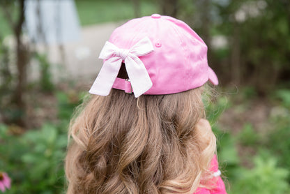 Girl wearing a pink baseball hat with a pink bow on the back