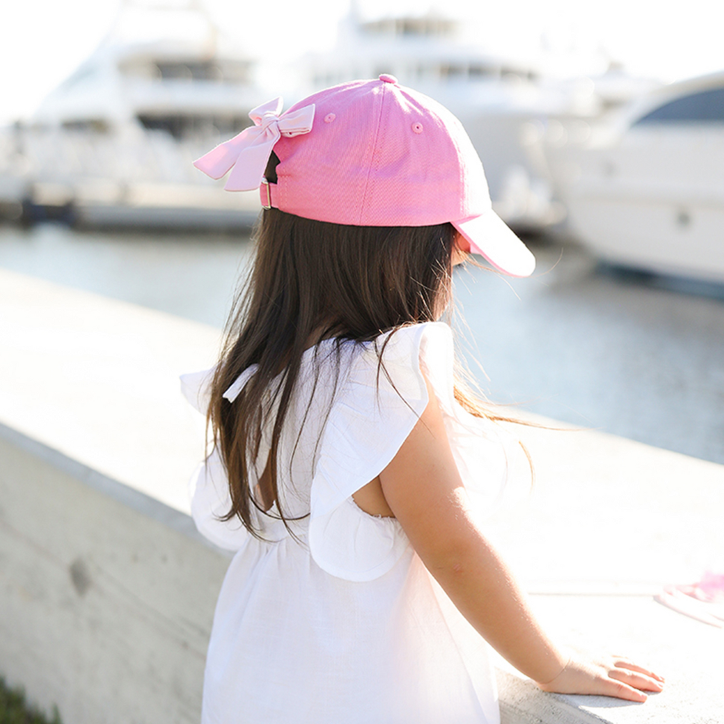 Girl wearing a pink baseball hat with a pink bow on the back