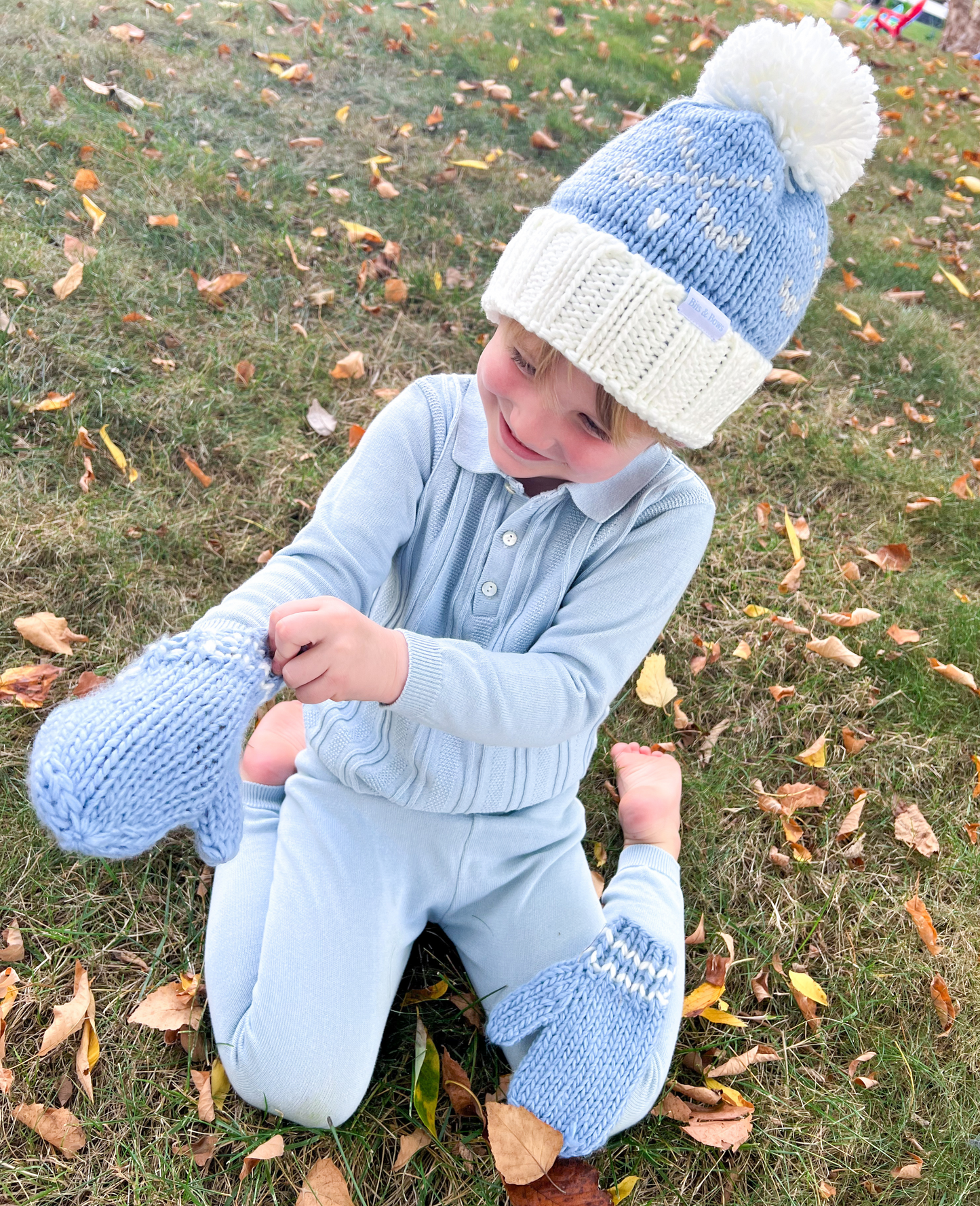 Boy wearing a bobble hat and putting on blue mittens