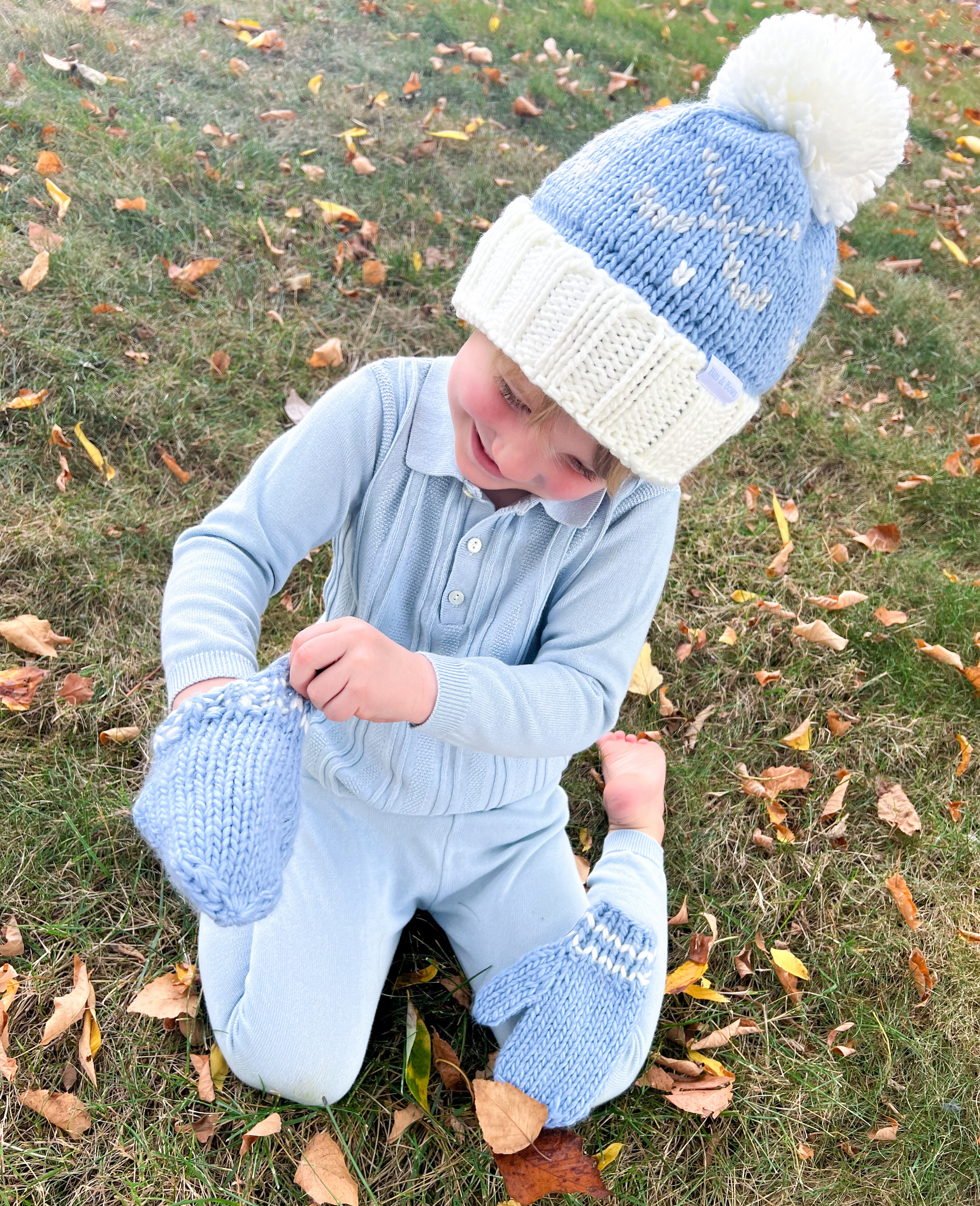 Boy wearing a bobble hat and putting on blue mittens