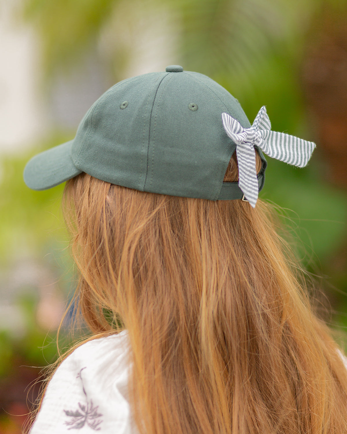 Girl wearing a green baseball hat with a green and white seersucker bow on the back