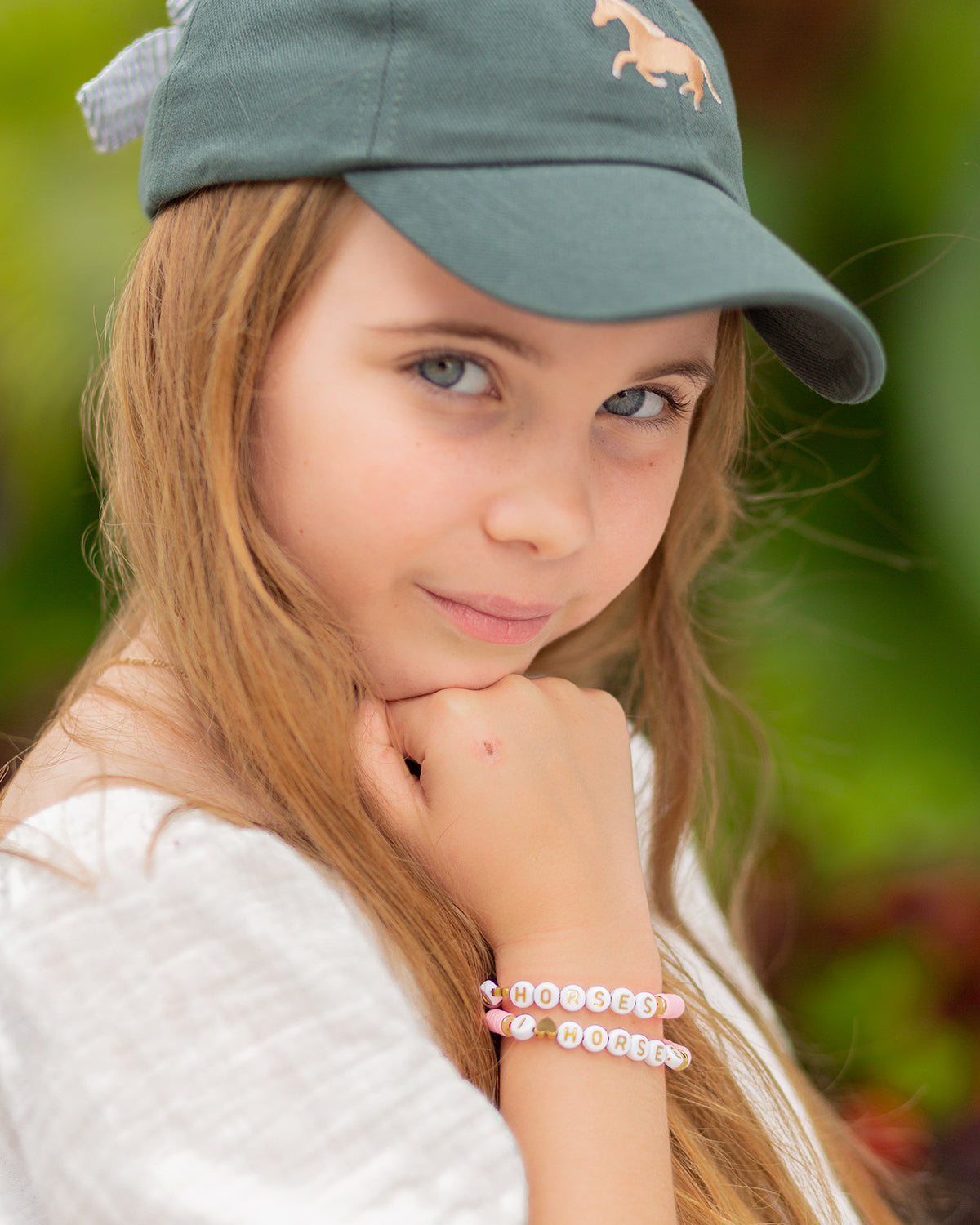 Girl wearing a green hat with horse embroidery and a horse word bracelet