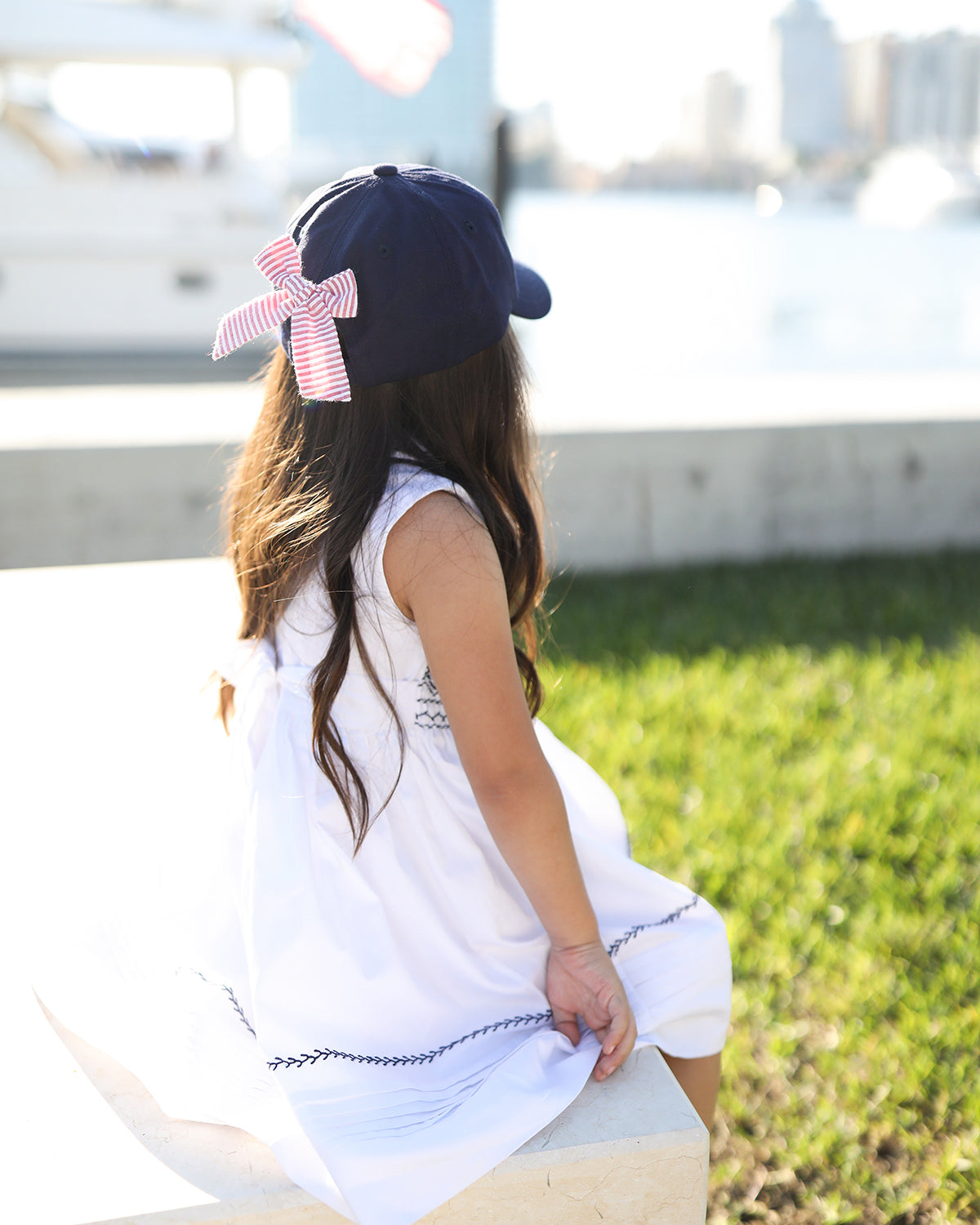 Girl wearing a navy blue baseball hat with a red and white seersucker bow on the back