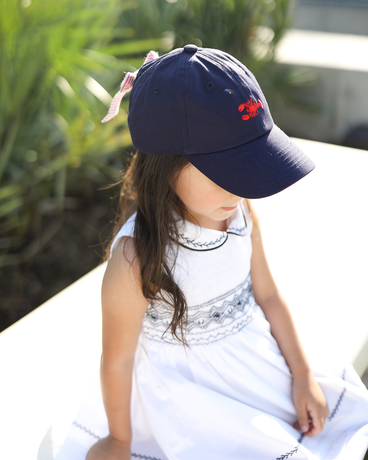 Girl wearing a navy blue baseball hat with lobster embroidery and a bow on the back