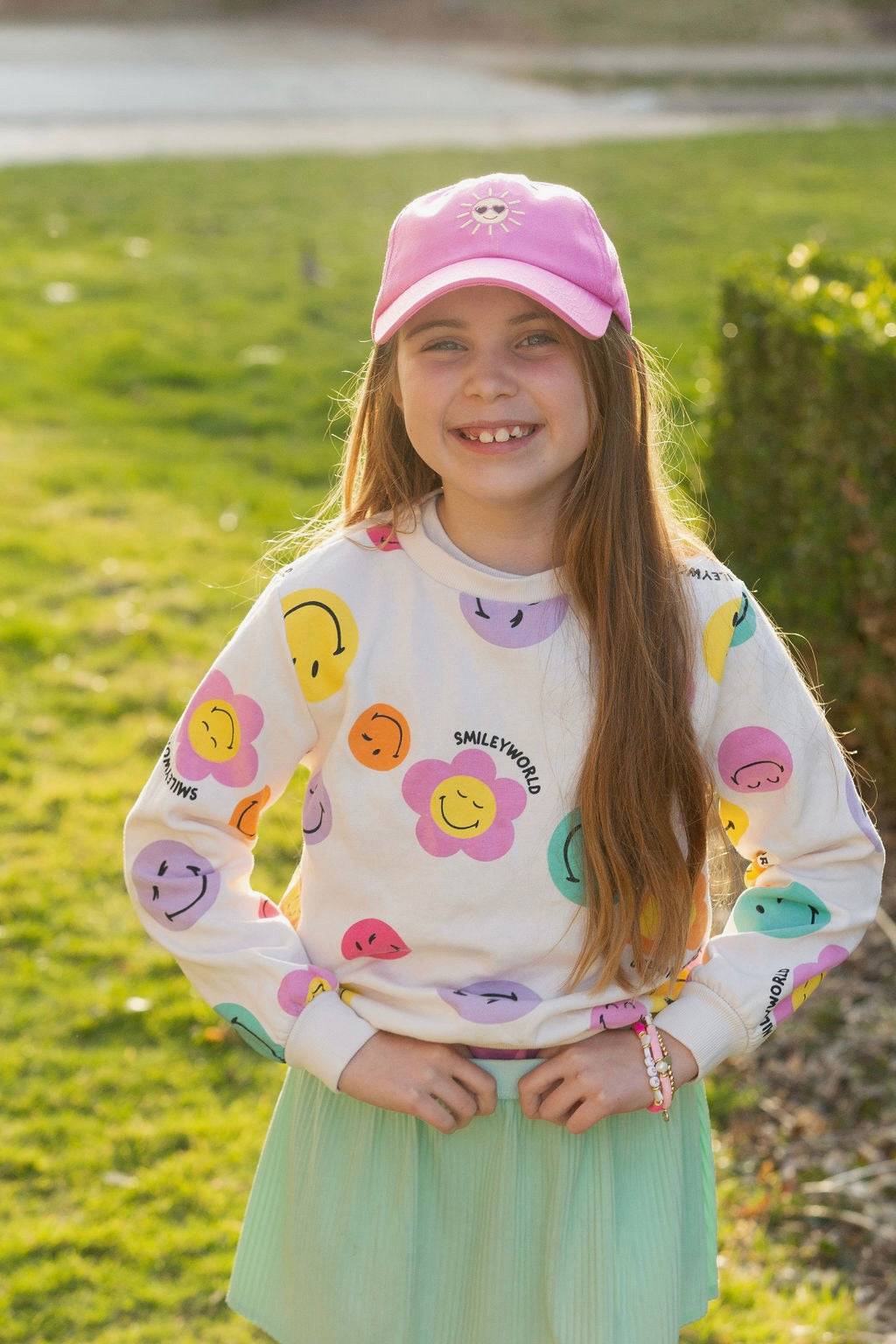 Girl wearing pink baseball hat with sun embroidery and pink bracelets