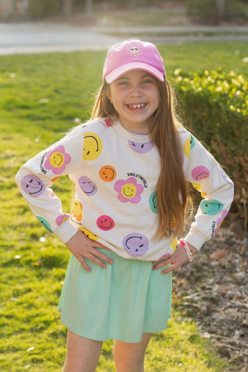 Girl wearing pink baseball hat with sun embroidery and pink bracelets