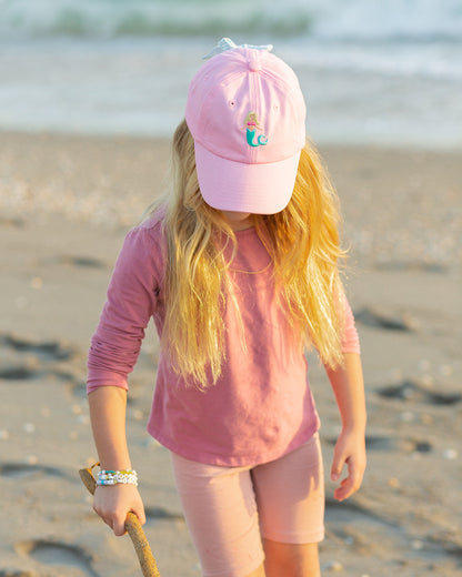 Girl wearing a pink baseball hat with mermaid embroidery and a bow on the back