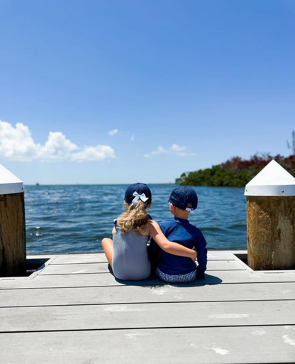 Little boy and girl sitting on a dock wearing coordinating navy blue baseball hats