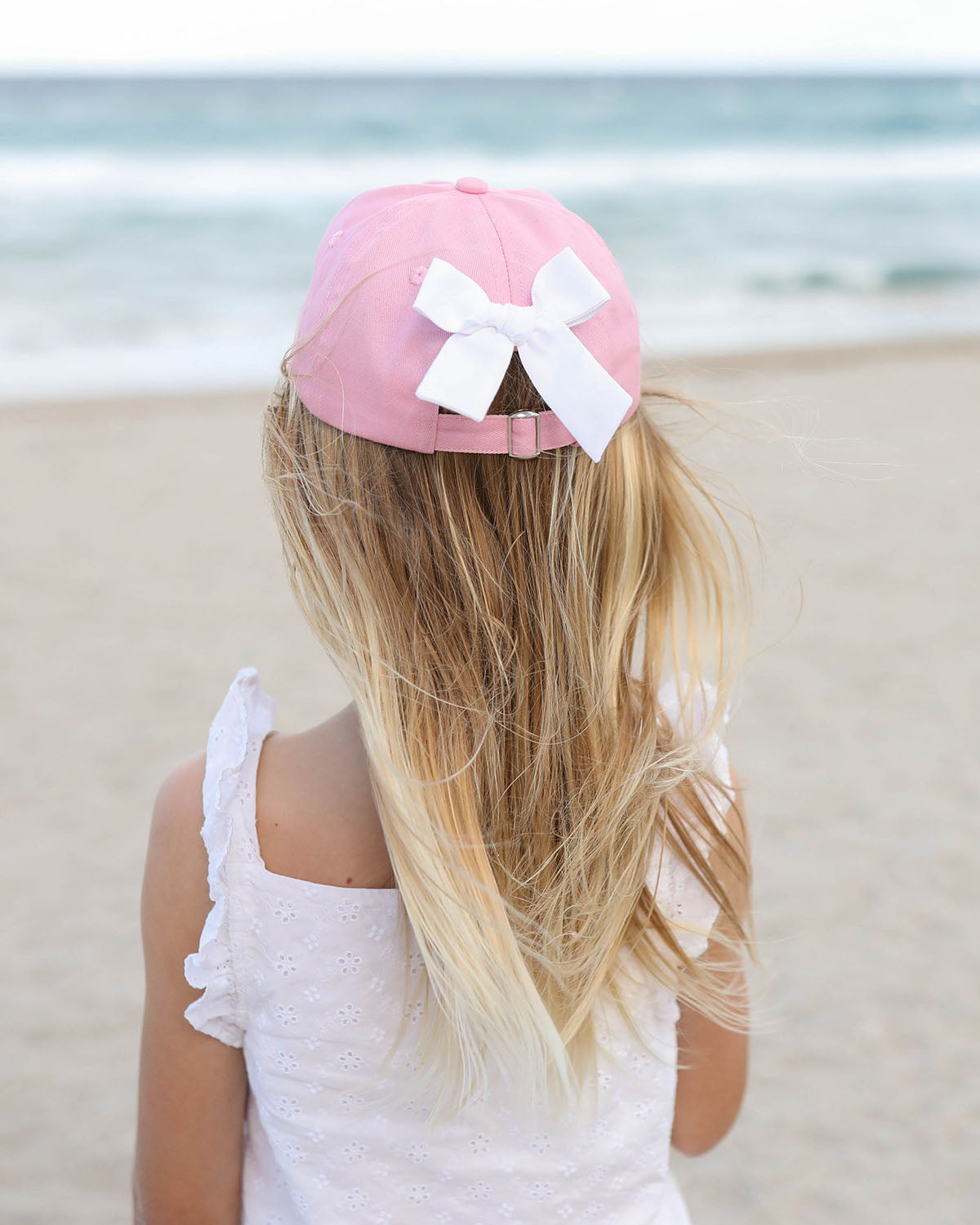 Girl wearing a pink baseball hat with a white bow on the back