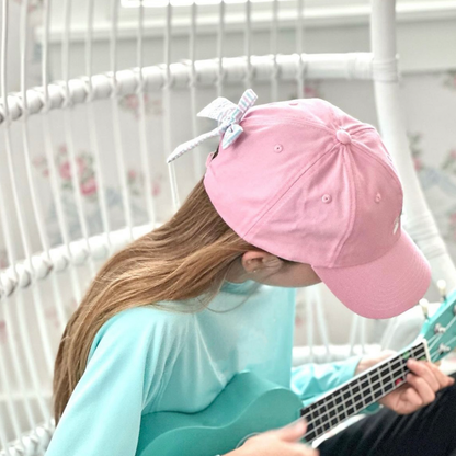 Girl wearing a pink baseball hat with a pink, blue and white seersucker bow on the back