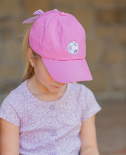 Girl wearing pink baseball hat with soccer ball embroidery and a bow on the back