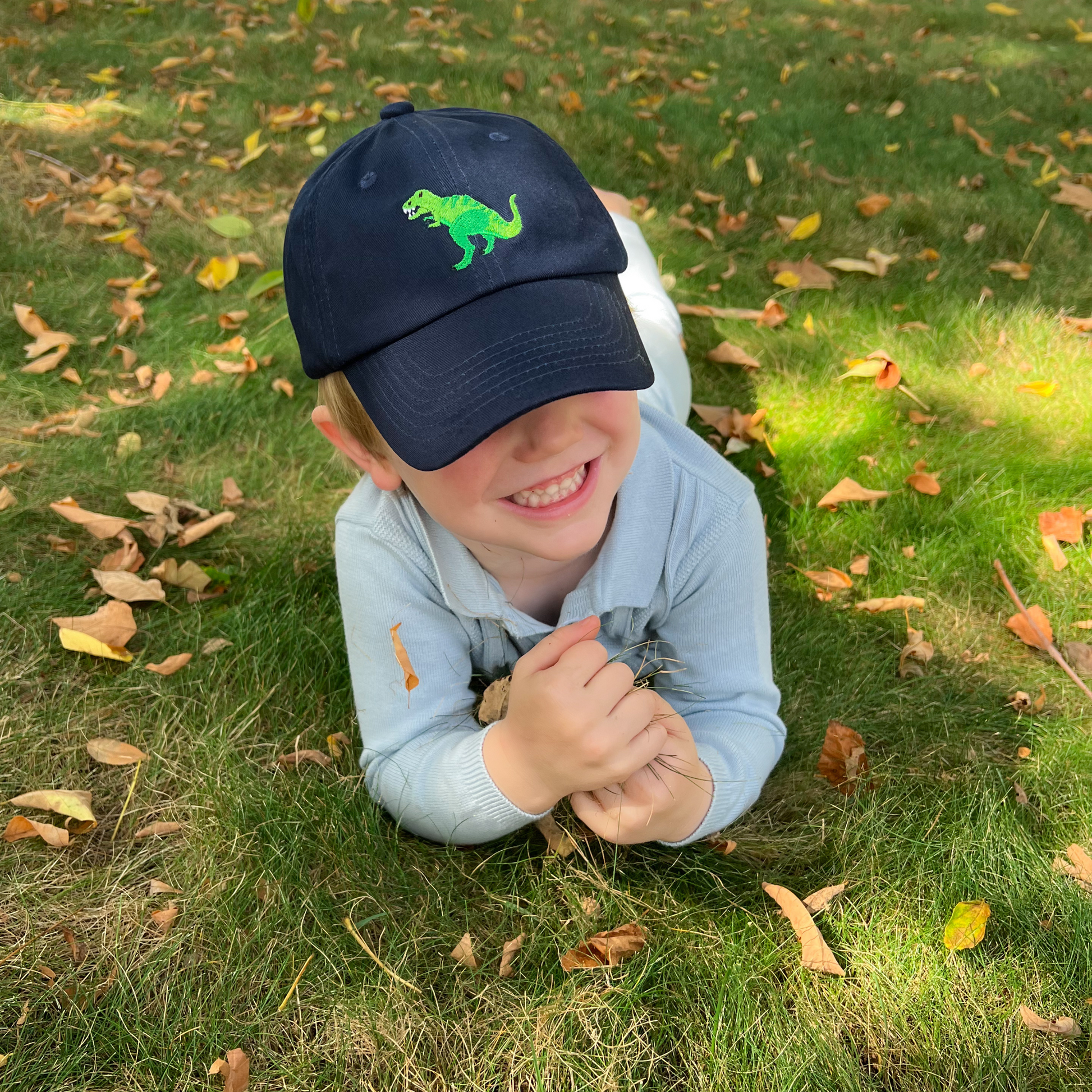 Boy wearing a navy blue baseball hat with t-rex motif embroidery