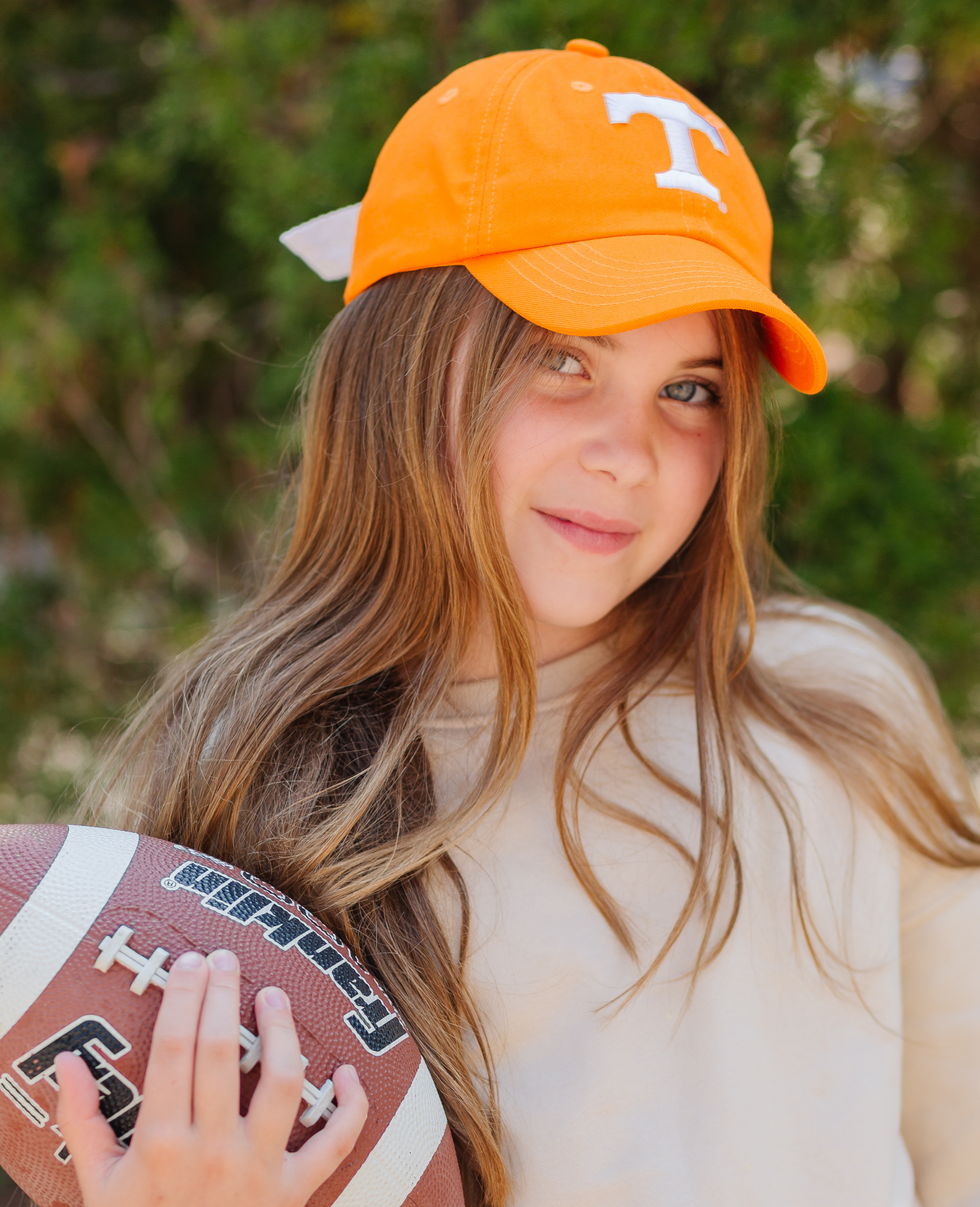 Girl holding a football and wearing an orange Tennessee Vols baseball hat