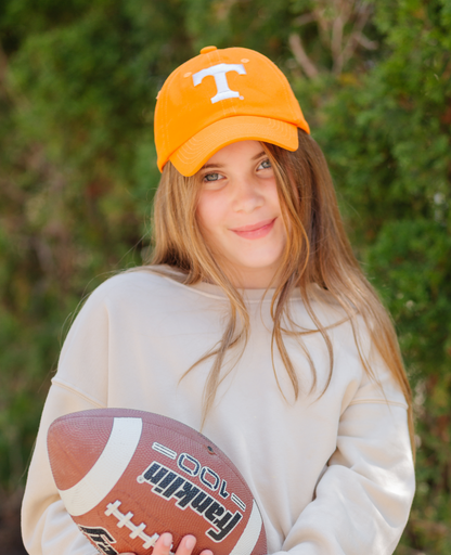 Girl holding a football and wearing an orange Tennessee Vols baseball hat