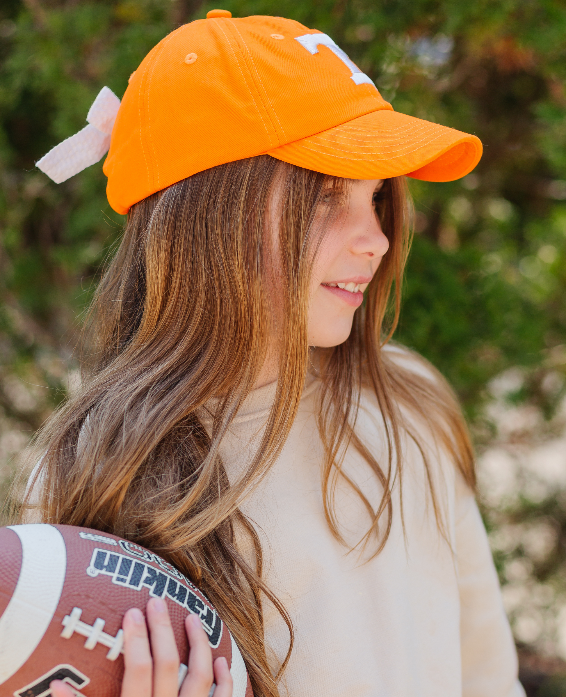 Girl holding a football and wearing an orange Tennessee Vols baseball hat