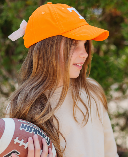 Girl holding a football and wearing an orange Tennessee Vols baseball hat