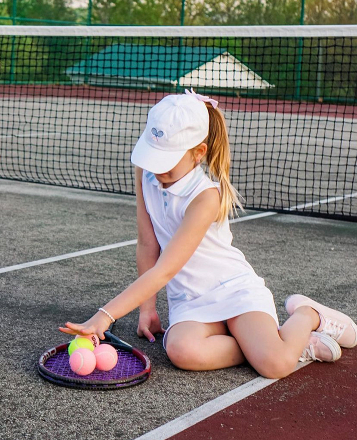 Girl wearing a white baseball hat with tennis racket embroidery and a bow on the back