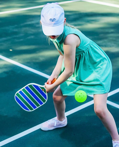 Girl wearing a white baseball hat with tennis racket embroidery and a bow on the back