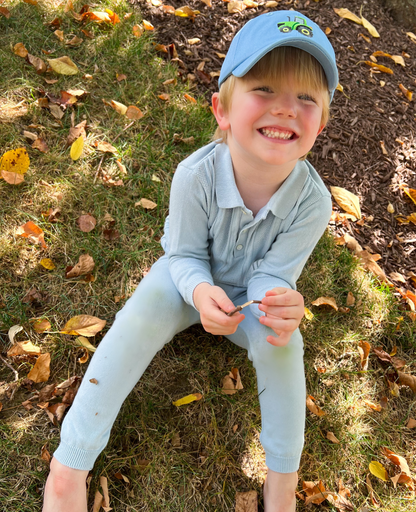 Boy wearing a blue baseball hat with   tractor motif embroidery