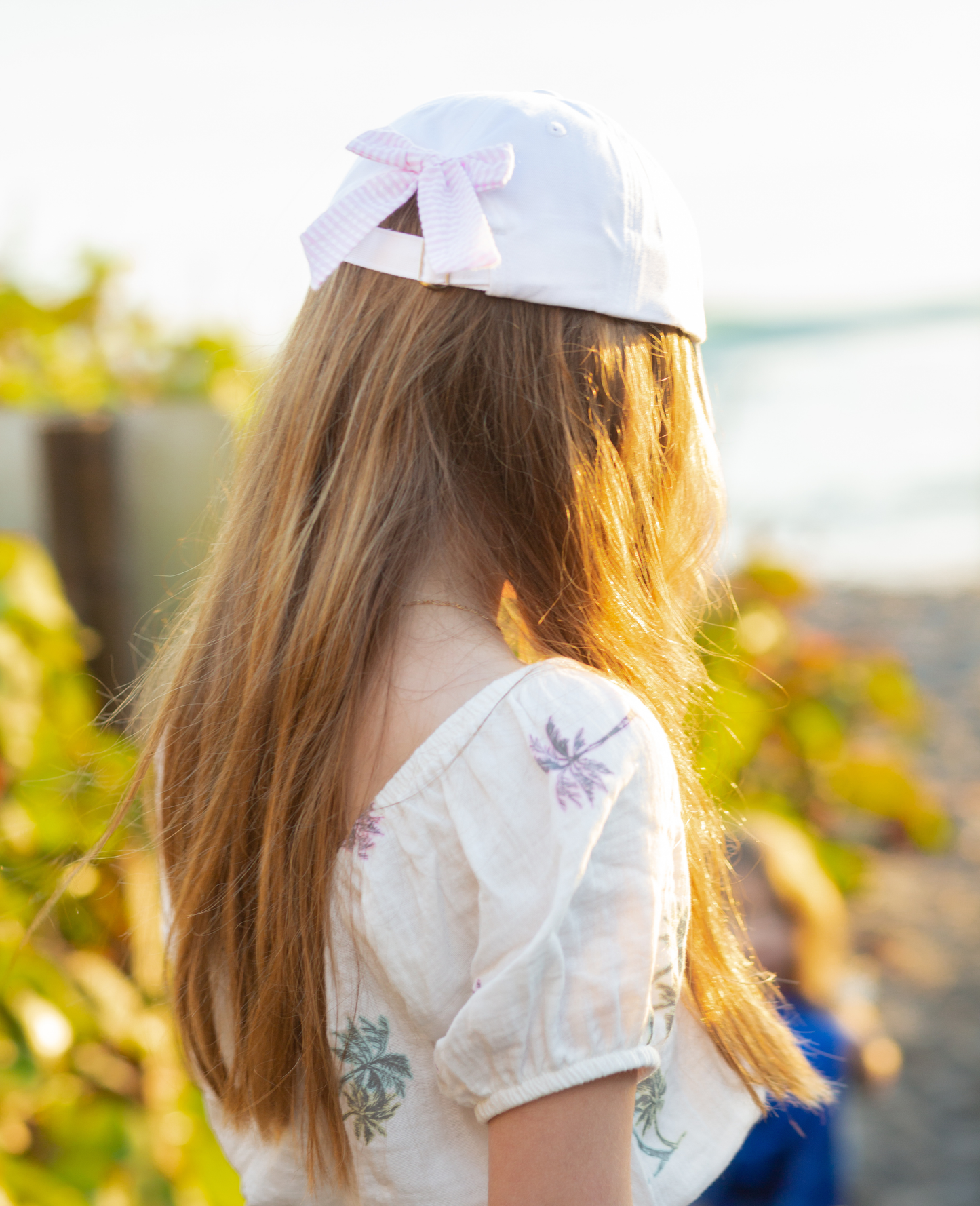 Girl wearing a white baseball hat with a pink and white seersucker bow on the back